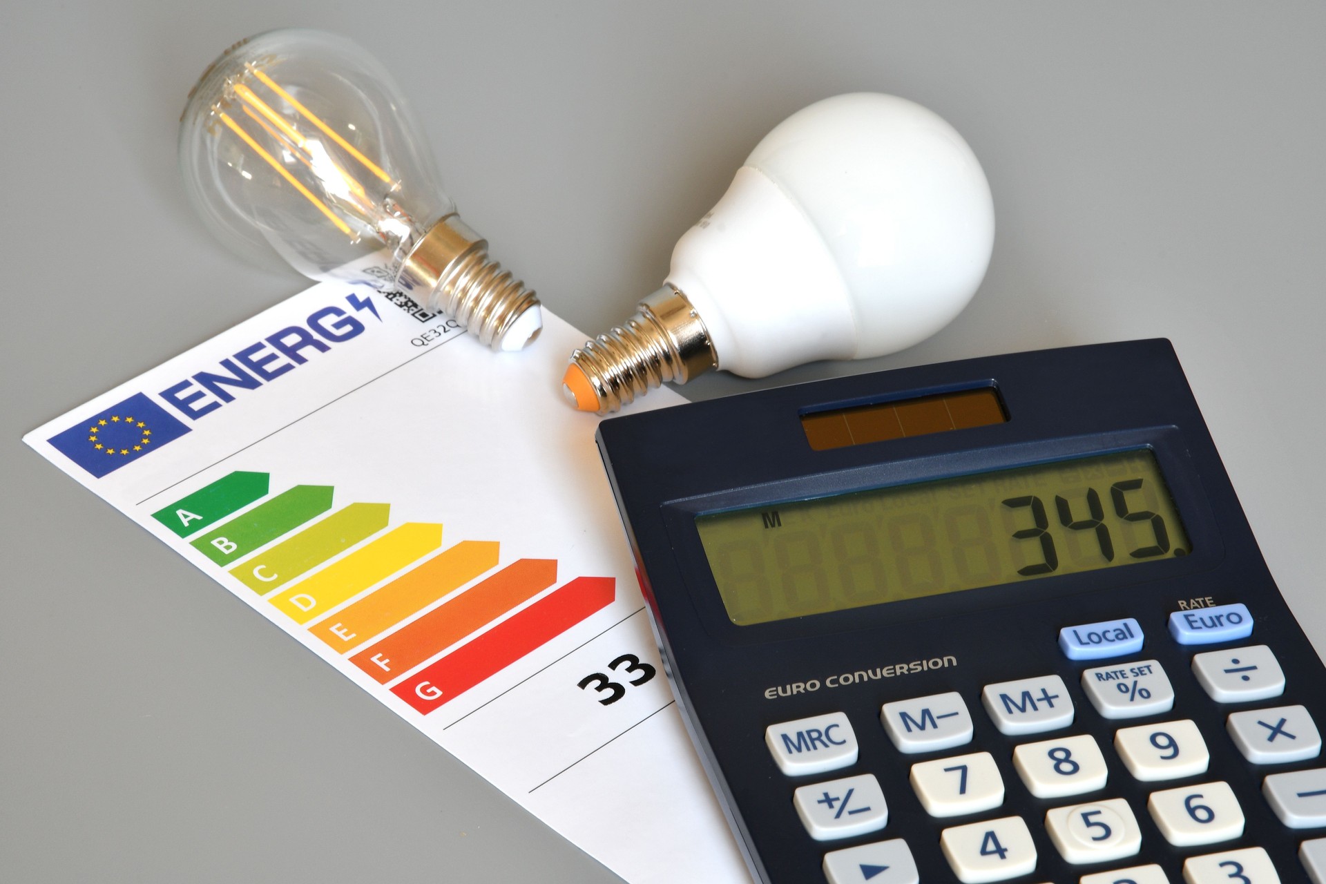 Energy efficiency rating table with light bulbs and calculator on gray background, close-up. Concept for Energy price increase.